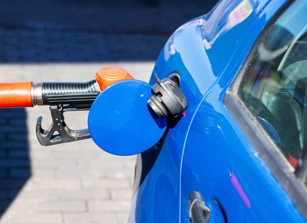A blue car is currently being filled up with gas at a gas station A blue car is currently being filled with gasoline at a busy gas station, ensuring it has enough fuel for its next journey ahead